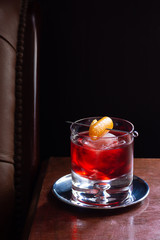 Negroni Cocktail, with Gin, Red Vermouth, and Campari, over Ice with Orange Twist in Dark Luxurious Bar with Copy Space