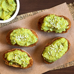 Fototapeta na wymiar Toasted bread slices with green pea and parsley spread garnished with white sesame seeds, photographed overhead with natural light (Selective Focus, Focus on the top of the spread on the breads)