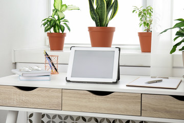 Tablet on table and houseplants in office interior, space for text