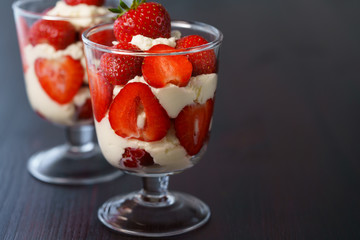 Whipped cream and strawberries served in a glass. Dark wooden table, high resolution