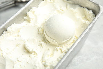 Container with delicious vanilla ice cream on table, closeup