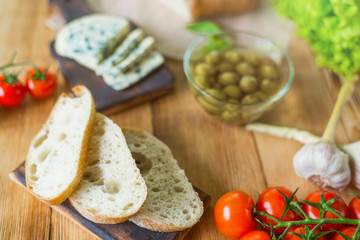 Ingredients for cooking bruschetta: chopped ciabatta, olives, tomatoes, blue cheese on a wooden background. Cooking healthy and tasty food.