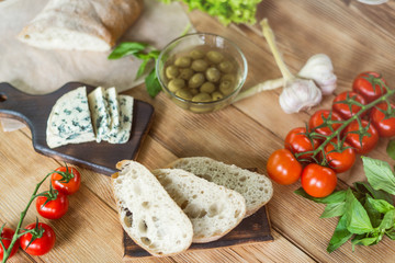 Ingredients for cooking bruschetta: chopped ciabatta, olives, tomatoes, blue cheese on a wooden background. Cooking healthy and tasty food.