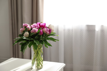 Vase with bouquet of beautiful peonies on table in room, space for text