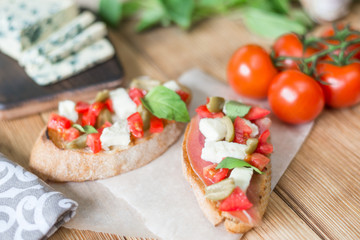 Traditional Italian bruschetta with blue cheese, feta, tomatoes, basil leaves, jamon on a wooden background.