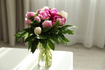 Vase with bouquet of beautiful peonies on table in room, space for text