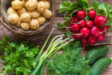 Fresh raw organic vegetables: potatoes, radishes, green onions, cucumbers on a wooden background.