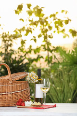 Picnic basket and wine with products on table against blurred background, space for text