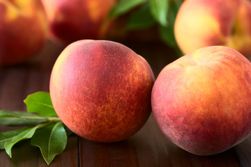 Fresh ripe peaches, photographed on dark wood with natural light (Selective Focus, Focus on the front of the front left peach)