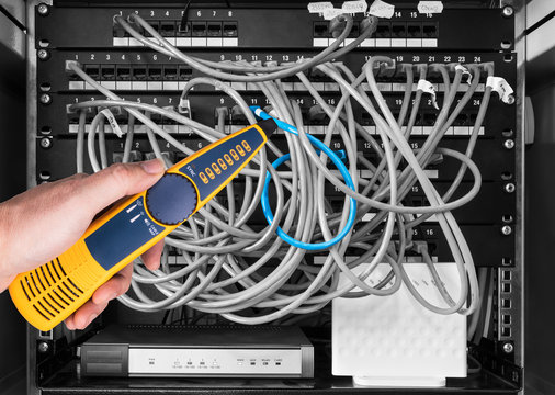 Network cable tester detail. Measuring probe in hand of expert on black and white background. Professional measurement of structured cabling in patch panels of rack case by yellow device. IT service.