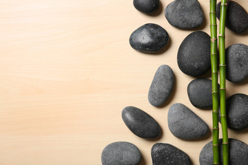 Spa stones with bamboo stems on wooden background, top view. Space for text