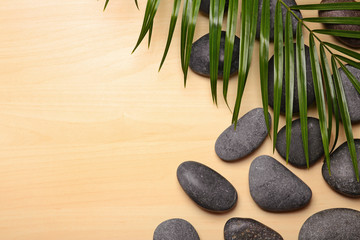 Spa stones with palm leaf on wooden background, top view. Space for text