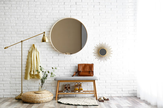 Hallway interior with big round mirror and shoe storage bench near brick wall