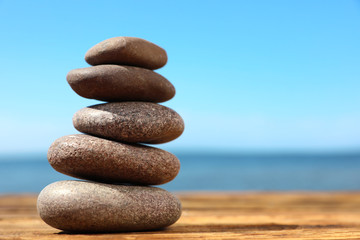 Stack of stones on wooden table against seascape, space for text. Zen concept