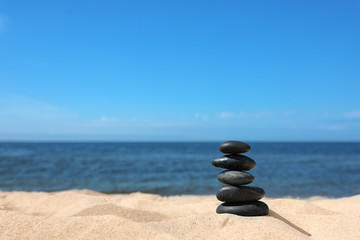 Stack of stones on sand near sea, space for text. Zen concept