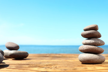 Stack of stones on wooden table against seascape, space for text. Zen concept
