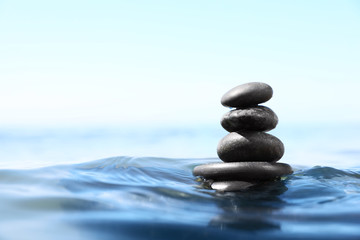 Fototapeta na wymiar Stack of stones in sea water, space for text. Zen concept