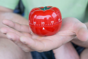 Mechanical red tomato kitchen timer set to 25, held by one open hand