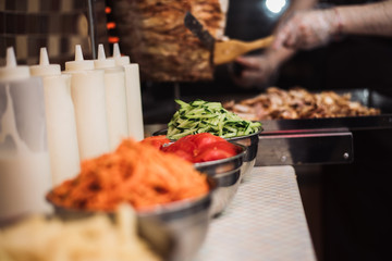 Drinks with tomatoes, cucumbers, Korean carrots and french fries, sauce dishes on the background of kebabs and fried chicken meat for shawarma.