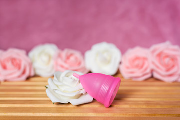 Obraz na płótnie Canvas Menstrual cup from a medicinal silicone. Pink and white roses. Concept of take care of woman health and zero waste solution for intimate hygiene.