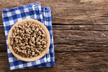 Raw dehydrated soy meat, soy protein, soya chunks or textured vegetable protein on wooden plate, photographed with copy space overhead on rustic wood