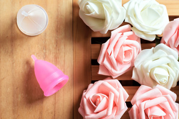 Top view of menstrual cups from a medicinal silicone. Pink and white roses. Concept of take care of woman body and health. Zero waste.