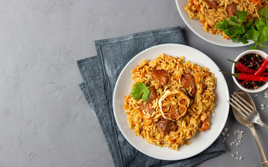 Asian dish - pilaf from from rice, vegetables and meat in a plate on gray background. Top view with copy space.
