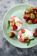 Traditional English dessert Eton mess with raw strawberries, cream and meringues in glasses in green plate
