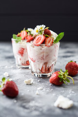 Healthy dessert on English cuisine. Eton mess with strawberries, cream and meringues in glasses on black and gray background