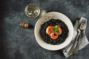 Delicious Italian risotto with grilled big tails of shrimp and cuttlefish ink (squid-ink). Black risotto. Healthy tasty food.  Top view. Copy space. 