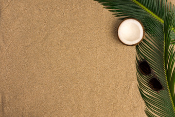 Fototapeta na wymiar Beach theme on the sand background. Palm leaves, coconut, sunglasses on the sand. Top view.