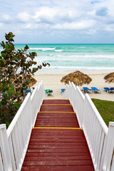 Naklejka premium Beautiful wooden ladder to the ocean beach. Beach with straw umbrellas and sun-loungers. Cloudy sky and blue water