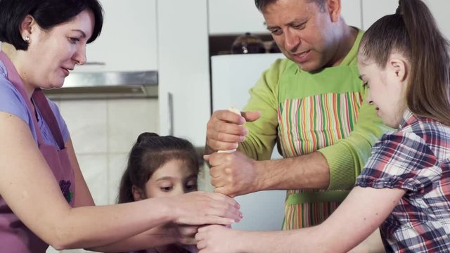 family prepares delicious meal and stretches thick dough roll above cooking table with equipment laughing closeup