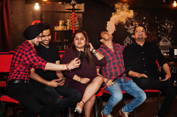 Group of indian friends sitting at lounge bar, having fun and rest, smoking hookah and looking on...