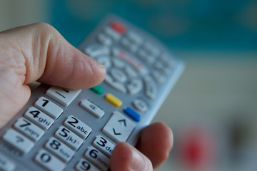 TV remote control held by human hand, turning volume down