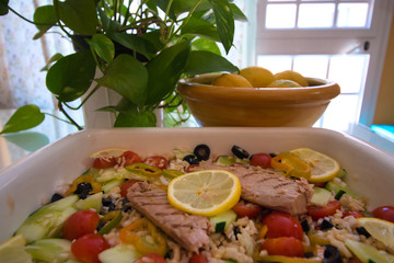 Tasty rice salad with fresh vegetables and grilled mackerel and in the background a bowl with lemons next to green leaves