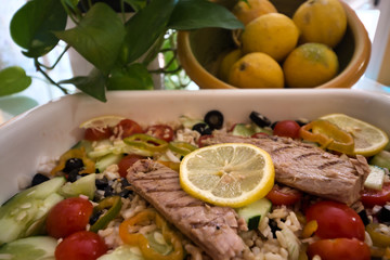 Tasty rice salad with fresh vegetables and grilled mackerel and in the background a bowl with lemons next to green leaves