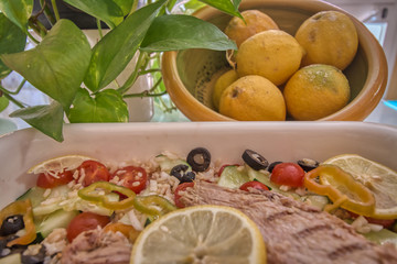 Tasty rice salad with fresh vegetables and grilled mackerel and in the background a bowl with lemons next to green leaves