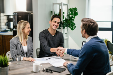 Happy couple shaking hands with their real estate agent at home.
