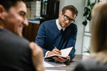 Financial advisor taking notes while communicating with a couple on a meeting.