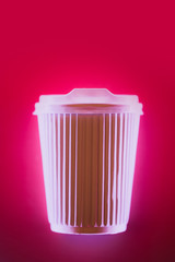 Close up of coffee to go cup in neon light on bright pink background.