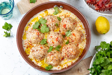 CRABMEATBALLS crab meatballs in white creamy sauce in red pan, whole king crab, cilantro, lemon and white wine on white background