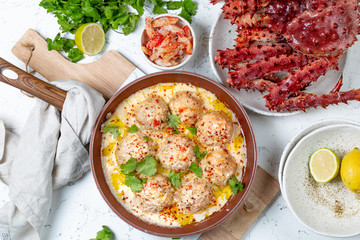 CRABMEATBALLS crab meatballs in white creamy sauce in red pan, whole king crab, cilantro, lemon and white wine on white background