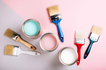 Three open cans of pastel paint with five brushes on pink and grey background.
