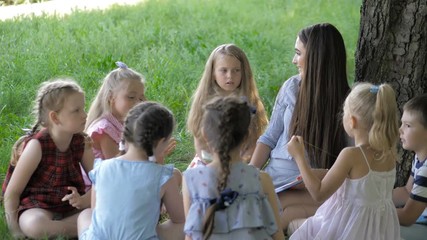 Children and education, young woman at work as educator reading book to boys and girls in park