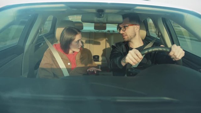 Young resentful woman quarreling with guy, screaming in car. Young people made up. Girl touching shoulder of boyfriend. Car driving. Indoors. Toxic relationship.