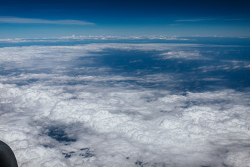 Plane window view with blue sky and beautiful clouds. As seen through window of an aircraft. View of wing & ocean. Airplane from city Bangkok to island Bali.