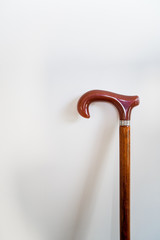 Wooden cane for seniors who need to lean on him to walk, leaning isolated on a white wall.