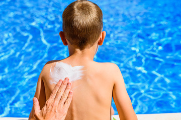 Woman spreads sunscreen on a child's back in summer to avoid sunburn.