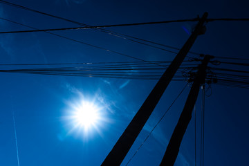Poles with electricity and telecommunications cables seen from below against the blue sky background.